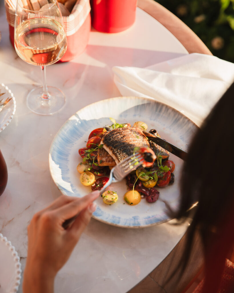 Plato de pescado con verduras y copa de vino servido en el Amù Beach Club del Hotel Gran Marbella.