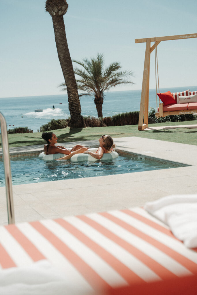 Dos personas relajándose en la piscina con vistas al mar y palmeras.